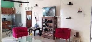 A living room with two red armchairs, a wooden cabinet, a television, and a kitchen area with cabinets and appliances. - Mavericks Convenient Cosy Loft in Dianis CBD (Diani Beach)