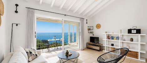 A modern living room with a large sliding glass door leading to a balcony with a sea view.