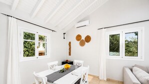 Een eethoek met een witte tafel, stoelen en uitzicht op groen buiten de ramen.