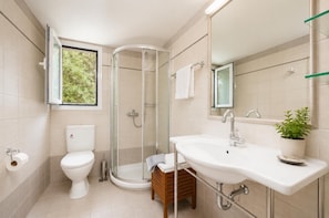 Een moderne badkamer met toilet, douche, wastafel en een plant in pot.