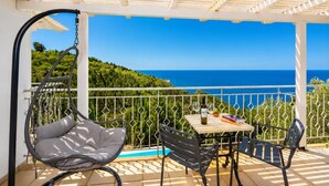 A balcony with a hanging chair, a table with a bottle and glasses, and a view of the sea.