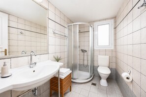 A bathroom with a sink, mirror, toilet, shower, and a small wooden stool.