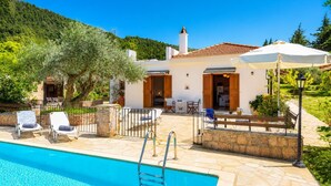 A villa with a swimming pool, outdoor seating, and a view of the surrounding hills.