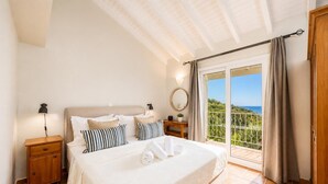 A bedroom with a bed, nightstands, a bedside table, a mirror, and a view of the outdoors. - Villa Gardenia - One Bedroom Villa, Sleeps 2 (Paxi)