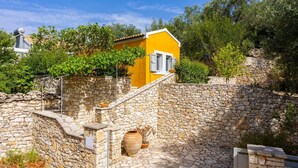 Une cour entourée de murs en pierre, avec un bâtiment jaune, un escalier en pierre et un grand pot en terre cuite.