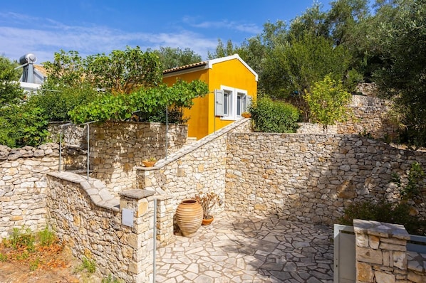 A stone-walled courtyard with a yellow building, a stone staircase, and a large terracotta pot.