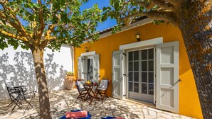 Une terrasse extérieure avec une table et des chaises, un transat et un arbre qui offre de l’ombre.