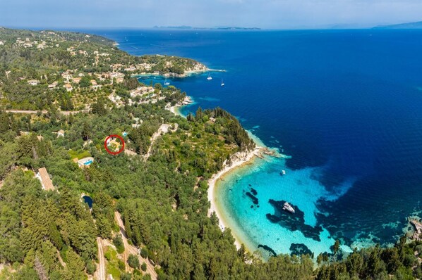 Vista aérea de una zona costera con playa, aguas azules cristalinas y una densa área boscosa.