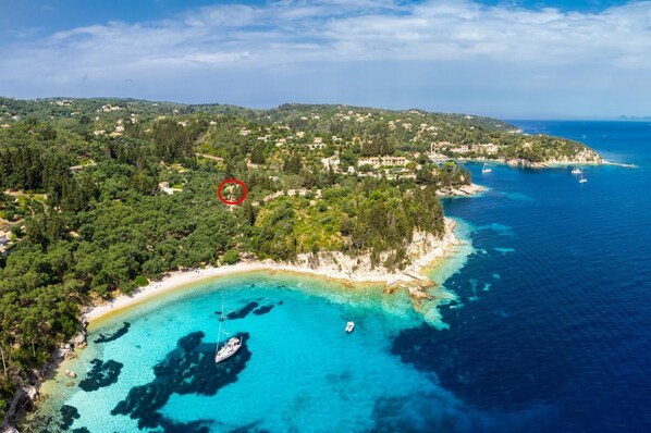 An aerial view of a coastal area with a beach, clear waters, and a red circled area indicating a specific location.