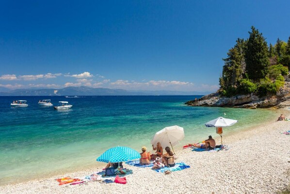 Relax on the beach with sun loungers and umbrellas, surrounded by turquoise waters and a rocky coastline.