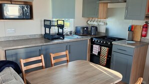 Cocina compacta con microondas, tostadora y estufa, una mesa de comedor con sillas y un sofá en la sala.