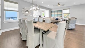 Ein geräumiges Wohnzimmer mit einem Holzessttisch, weißen Stühlen, einer Couch und einem Liegesessel.