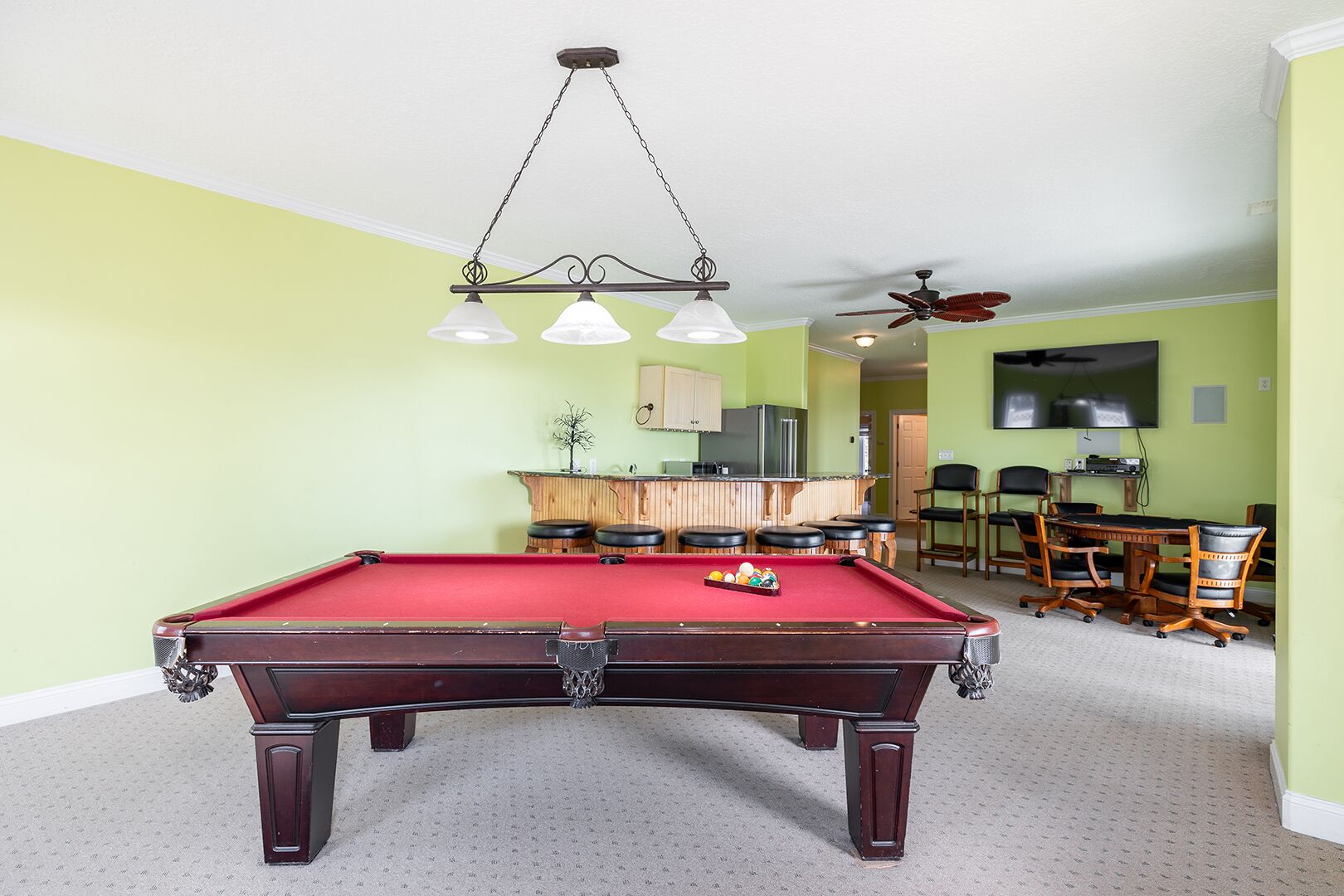 Een pooltafel met een rode viltkleed, een bar met krukken en een plafondventilator.
