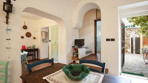 Un comedor con una mesa, sillas y un centro de mesa con un tazón verde. Se observa un televisor sobre un mueble en el fondo.