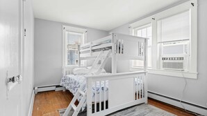A room with a bunk bed, a radiator, a window with blinds, and a door. - OCHG 6 10th Steet Top (Ocean City)