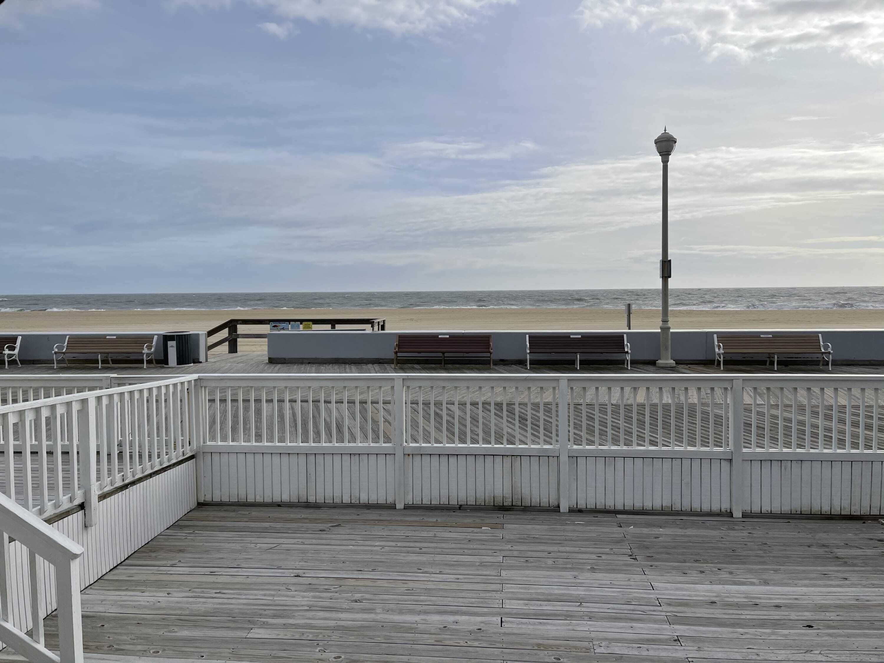 Una passerella di legno con panchine e un lampione, con vista su una spiaggia.
