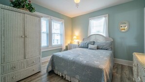 Un dormitorio con una cama grande, un armario, un ventilador de techo y una ventana con cortinas.
