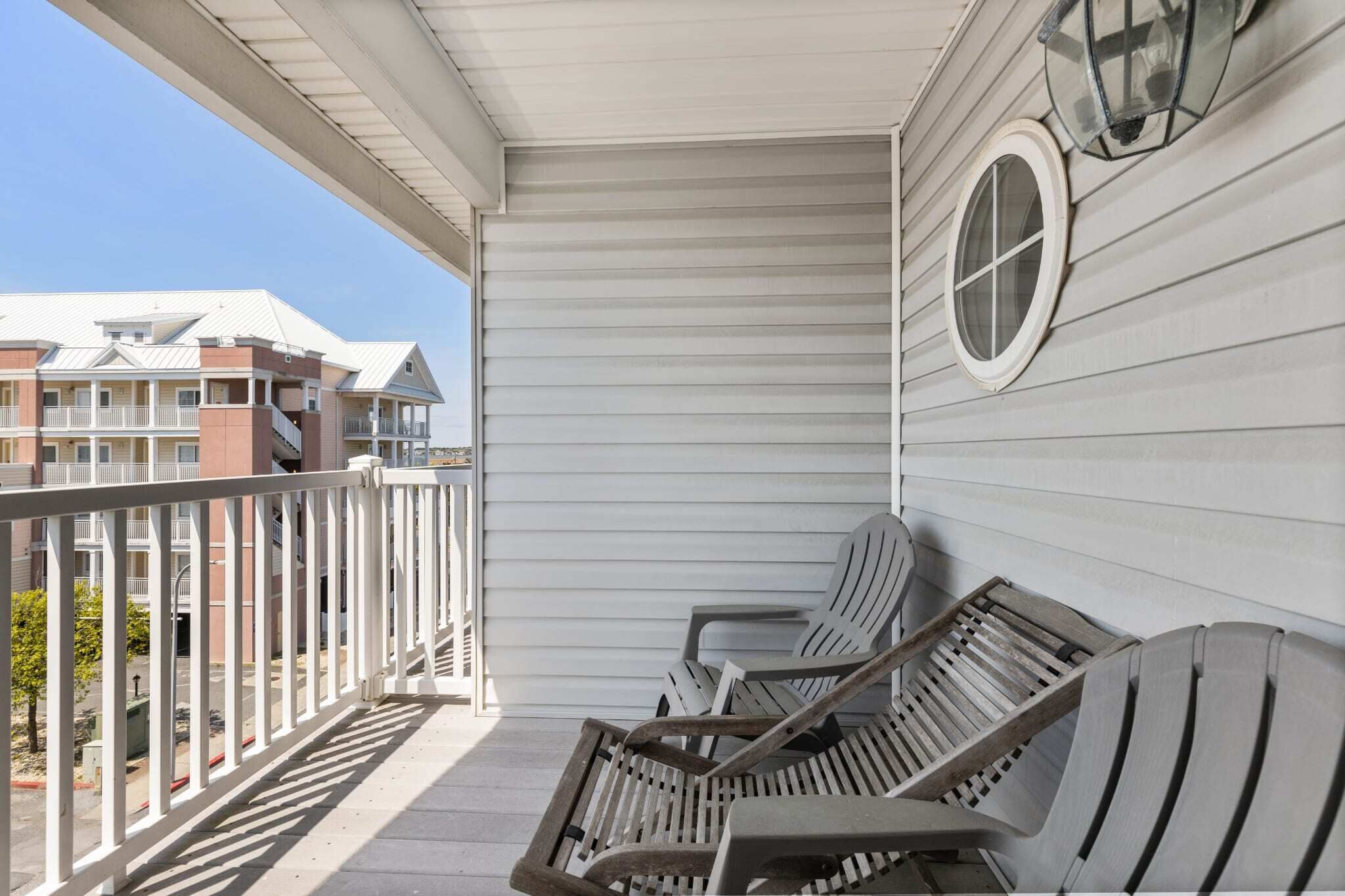 Un balcone con due poltrone Adirondack e un tavolo di legno, affacciato su una zona residenziale con case.