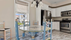 A kitchen with white cabinets, a stainless steel refrigerator, a microwave, and an oven. There is a round table with blue chairs and a chandelier above it.
