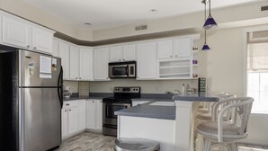 A modern kitchen with white cabinets, stainless steel appliances, and a bar area with white chairs.