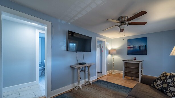 Un salon avec un ventilateur de plafond, un téléviseur à écran plat, une lampe et un tableau au mur.