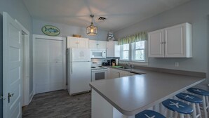 A kitchen with white cabinets, a refrigerator, a microwave, and a stove. There are bar stools with starfish designs.
