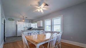 A kitchen with white cabinets, a wooden dining table, and a ceiling fan.