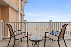 A balcony with two chairs and a small table, overlooking a beach.