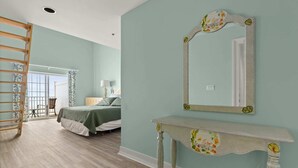 Quarto com cama, mesa de cabeceira, espelho, cômoda, escada e vista para outro quarto com janela e cadeira.