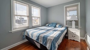 A bedroom with a bed, a nightstand, a lamp, and two windows with blinds.