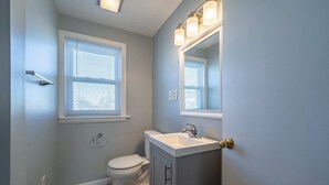 A bathroom with a toilet, sink, cabinet, and a mirror with lights.