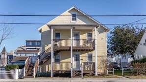 A two-story building with a balcony on the second floor, a front door, and a staircase leading to the entrance.