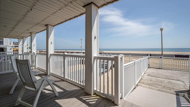 Een overdekt terras met witte relingen, een stoel en uitzicht op strand en zee.
