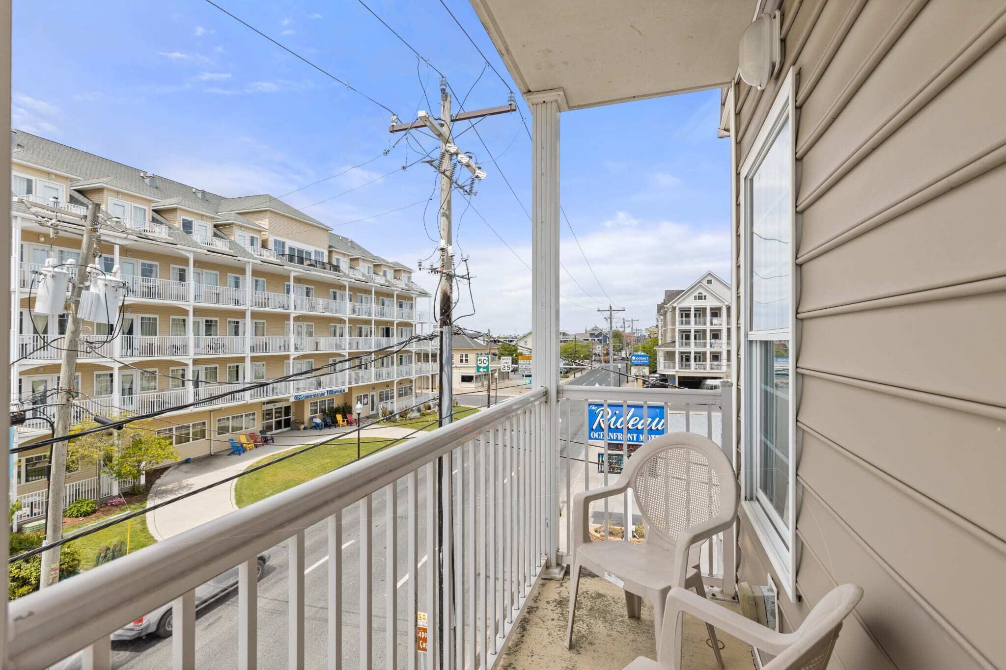 A balcony with a view of a multi-story building, a sign for 'Rideau Oceanfront', and a street with cars and a clear sky.