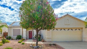 A residential property with a garage, a driveway, and a landscaped garden with a tree and various plants.