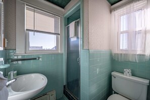 Um banheiro com pia branca, vaso sanitário e chuveiro com porta de vidro.