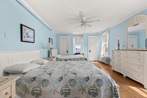 Quarto com duas camas, um ventilador de teto, cômoda e um quadro pendurado na parede.