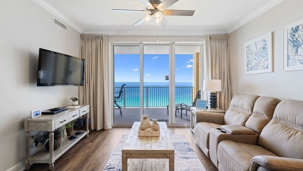A living room with a television, a sofa, a coffee table, and a view of the ocean through large glass doors. - Beautiful Tropic Winds Beachfront Condo 2BR,2BA Beach chair serv thru march- oct (Panama City Beach)