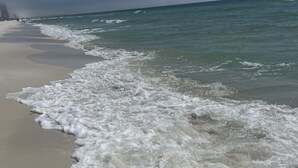 A beach with waves gently lapping onto the shore, a clear sky, and a distant pier. - Beautiful Tropic Winds Beachfront Condo 2BR,2BA Beach chair serv thru march- oct (Panama City Beach)