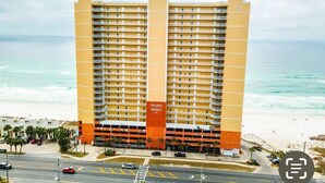 A high-rise hotel with multiple balconies, a parking garage, and a beach view. - Beautiful Tropic Winds Beachfront Condo 2BR,2BA Beach chair serv thru march- oct (Panama City Beach)