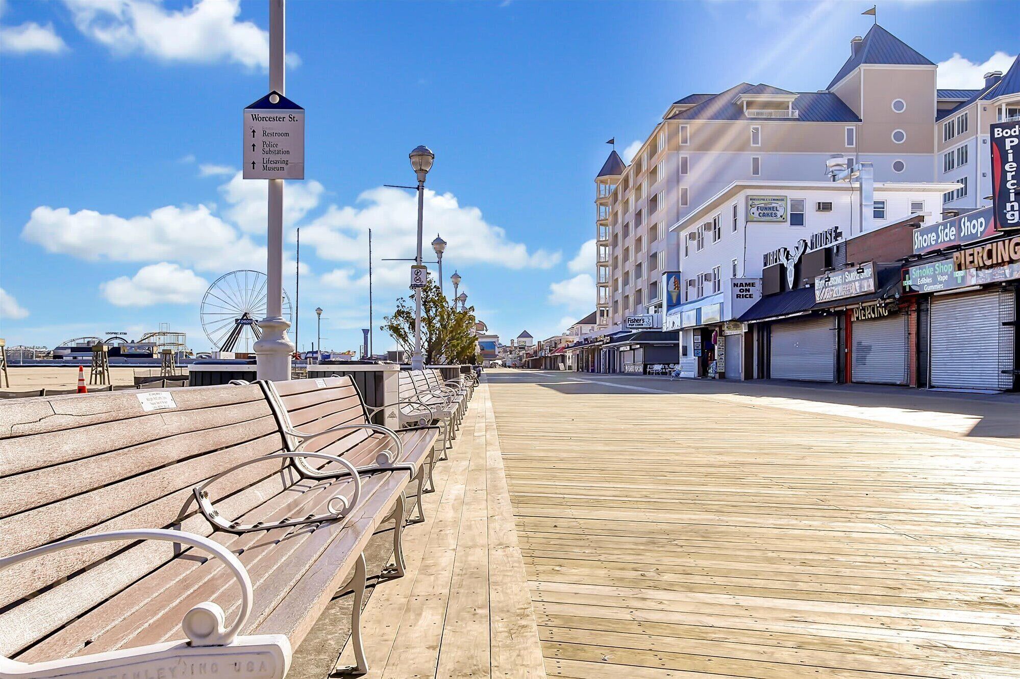 A boardwalk with benches, a signpost with directions to Worcester St., and a building with shops on the right.