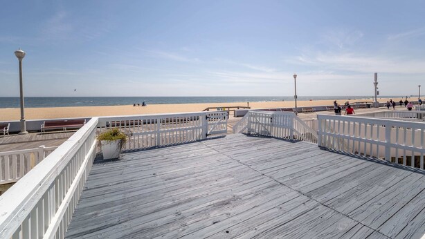 A wooden boardwalk leading to a beach with a clear sky. - OCHG Seafoam 1007 Sum (Ocean City)