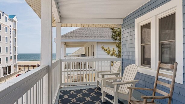 En balkong med en mönstrad matta, två Adirondack-stolar och utsikt över havet.