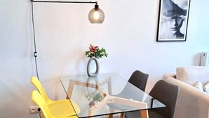Ein modernes Wohnzimmer mit einem Glastisch, zwei Stühlen, einer Couch, einer Wandlampe und einem gerahmten Kunstwerk.