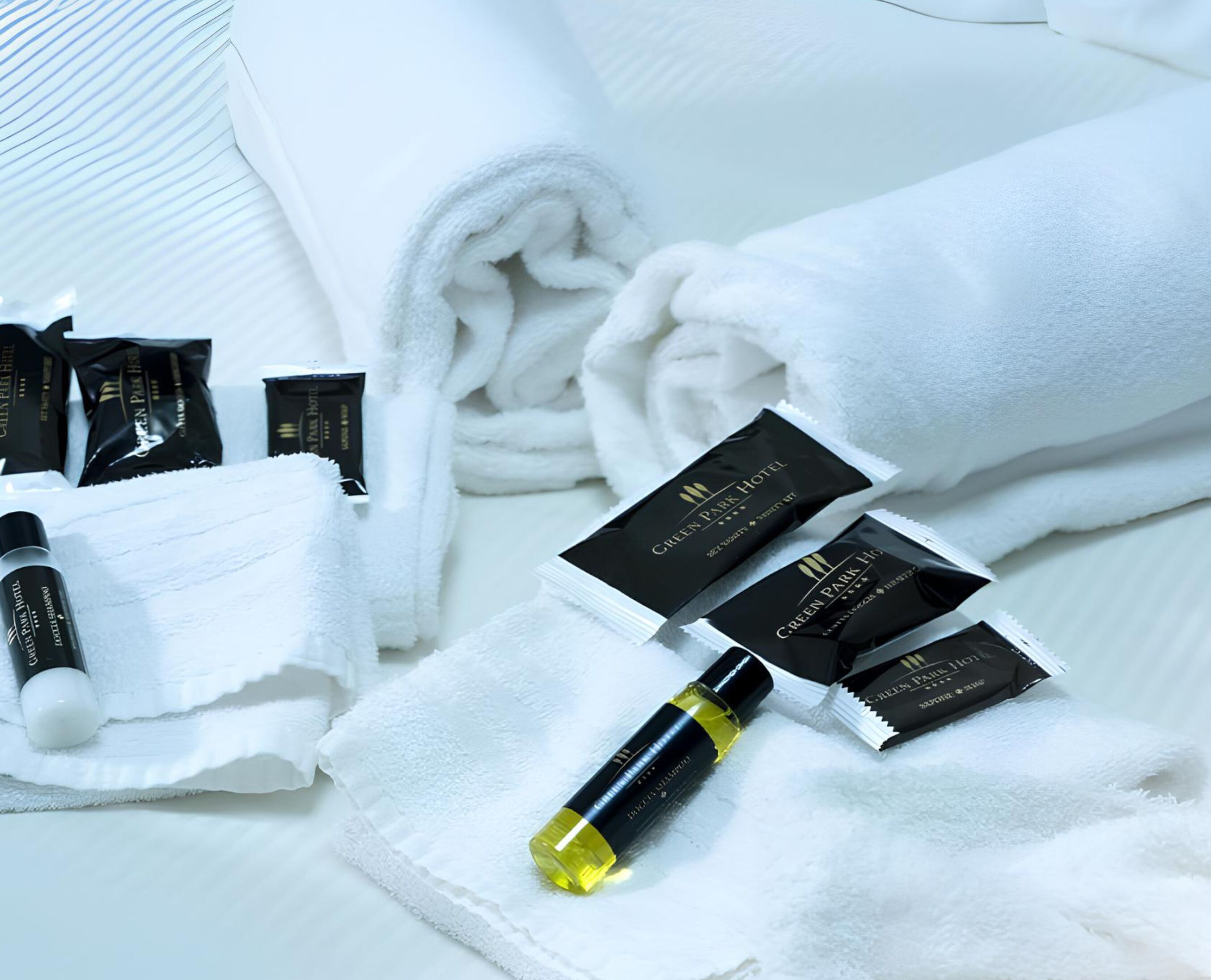 Neatly folded white towels, a bottle of lotion, and several small black boxes labeled "Green Park Hotel."