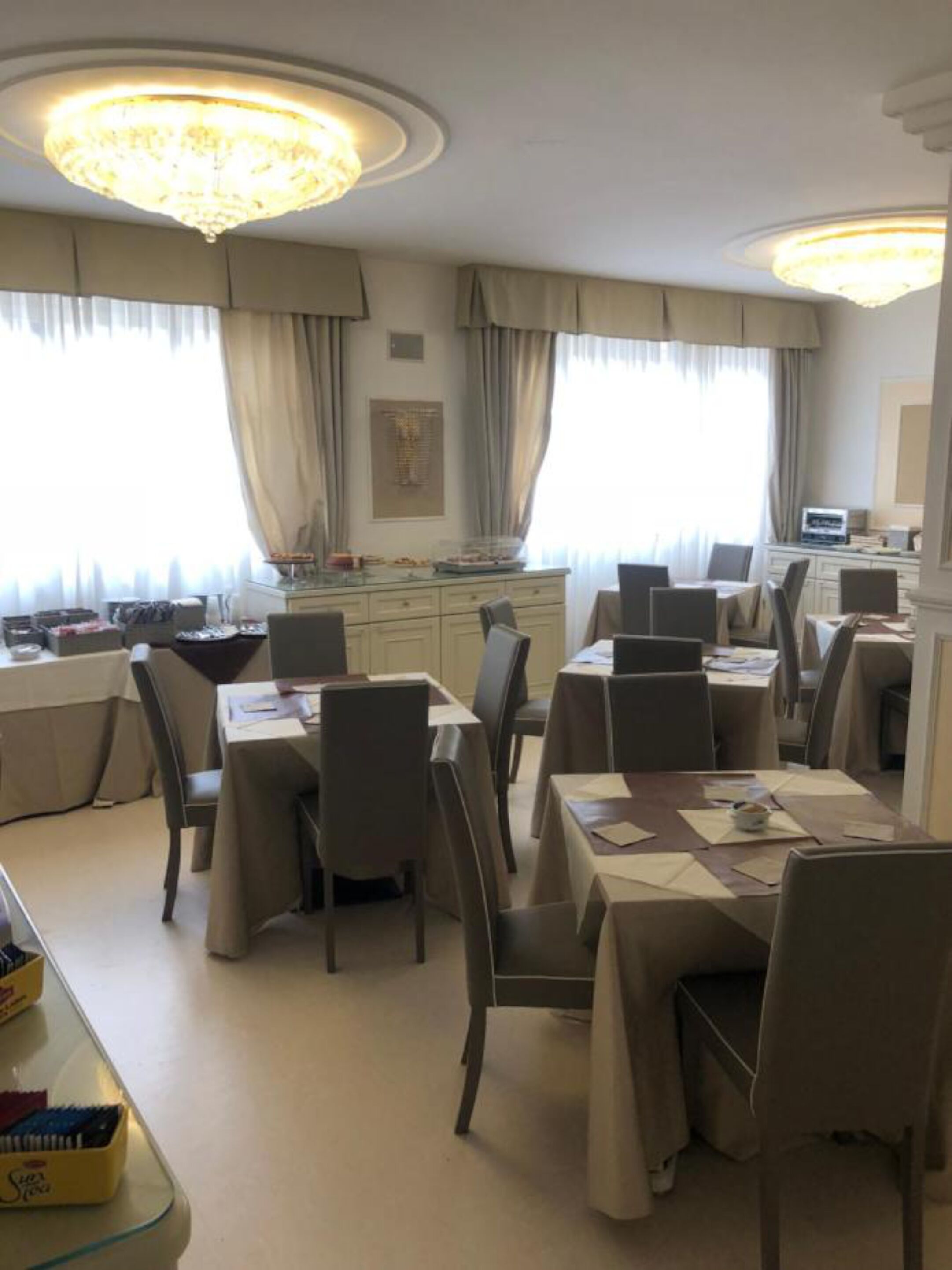 Un comedor con mesas y sillas, una araña y vistas al exterior a través de amplios ventanales.