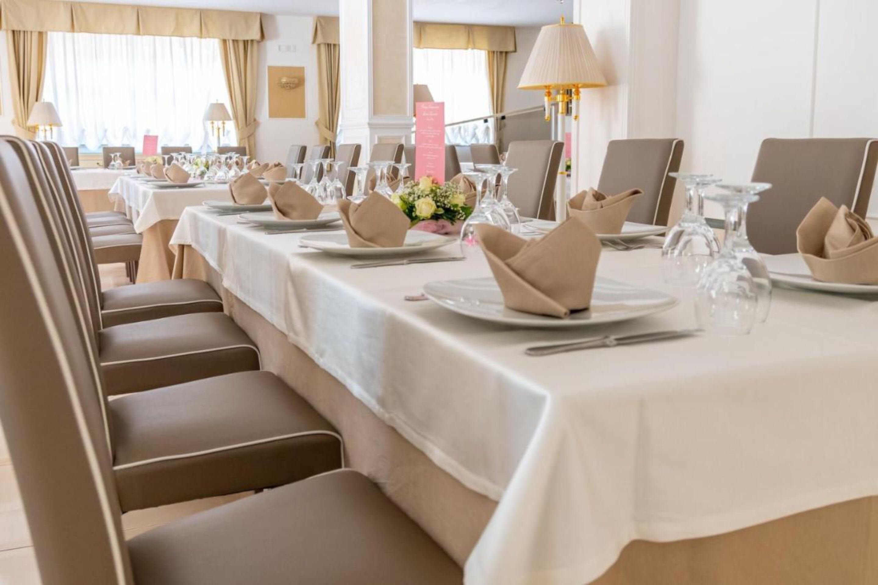 Un espace repas avec des tables dressées pour le service, agrémenté de nappes blanches, de serviettes de table beige et de verres transparents.