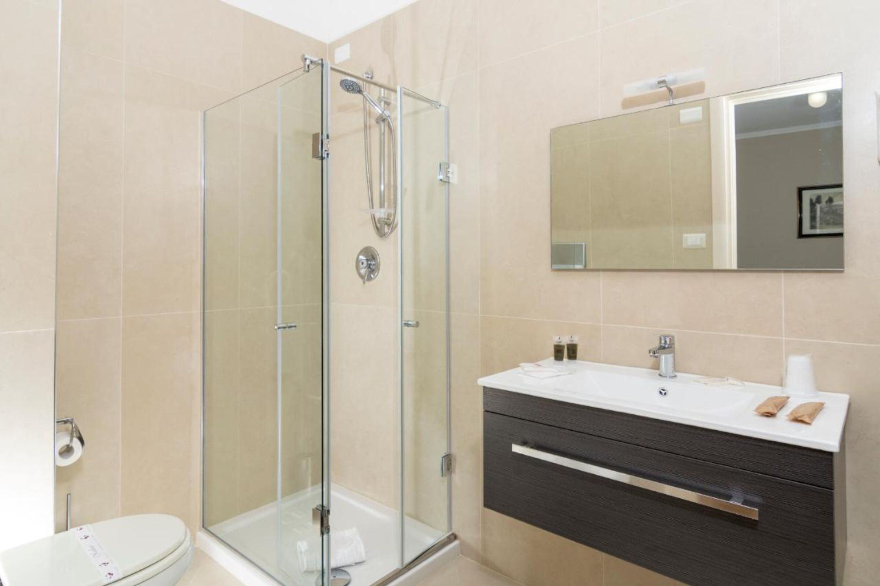 Un bagno moderno con doccia vetrata, lavandino bianco su mobile scuro e uno specchio grande.