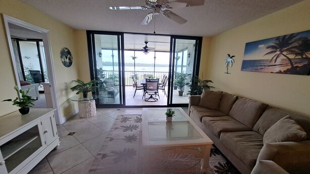 A living room with a sofa, coffee table, TV stand, and a balcony with outdoor furniture. - PALMS OF BAY BEACH-UNIT 1G

EXCEPTIONAL CORNER UNIT ON THE BAY WITH LARGE LANAI (Fort Myers Beach)