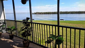 A balcony with potted plants, a hanging planter, and a view of a lake with a grassy area and a bench. - PALMS OF BAY BEACH-UNIT 1G

EXCEPTIONAL CORNER UNIT ON THE BAY WITH LARGE LANAI (Fort Myers Beach)